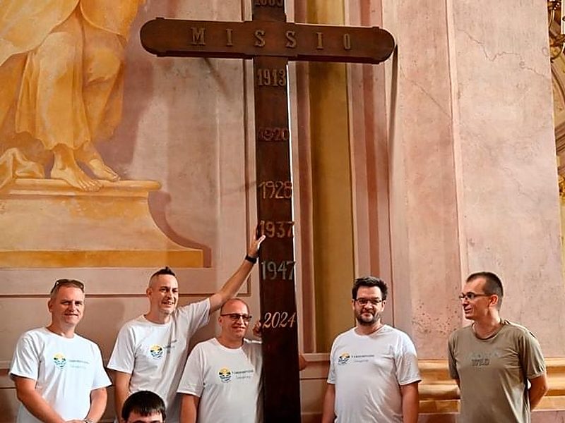 Hat férfi a templomi Missio-kereszt előtt, rajta az 1889-től 2024-ig tartó évszámokkal
