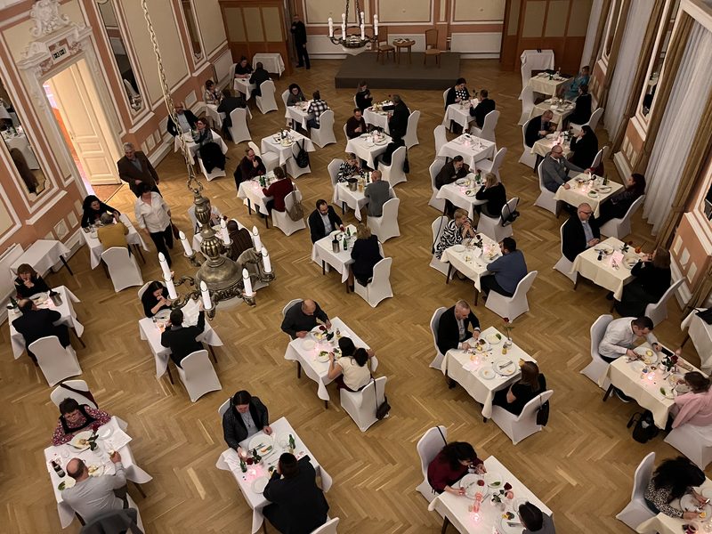 Madártávlati kép egy díszes bálteremről, terített asztaloknál vacsorázó párokkal